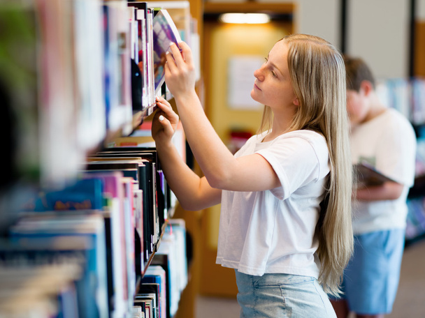 Teenage girl in library - Фото, изображение