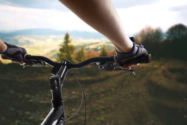 Mãos em luvas que mantêm o guiador de uma bicicleta. Mountain Bike ciclista montando pista única. Estilo de vida saudável atleta ativo fazendo esporte
 - Foto, Imagem
