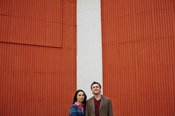 casal em casualwear em pé ao lado da parede vermelha
 - Foto, Imagem