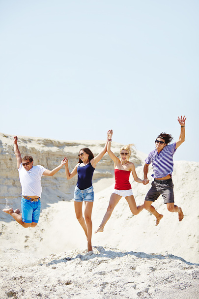 Nuoret hyppäävät hiekkarannan yli
 - Valokuva, kuva