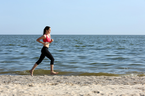Young woman jogging on beach - 写真・画像