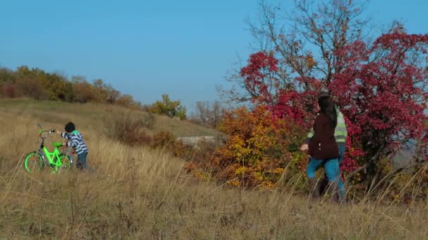 Familia joven feliz con un niño en bicicleta caminando en el prado de otoño
 - Imágenes, Vídeo