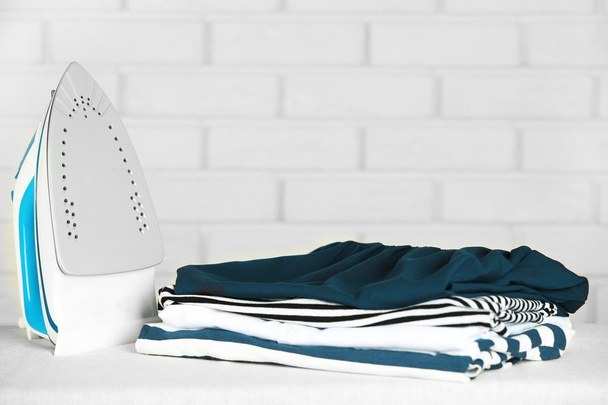 Pile of clothes and electric iron on brick wall background - 写真・画像