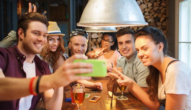 happy friends with smartphone taking selfie at bar - Photo, Image