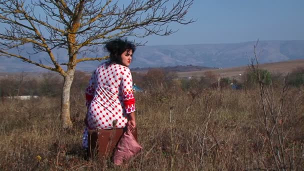 jovem mulher no branco pontilhado vestido sentado na mala na natureza
 - Filmagem, Vídeo