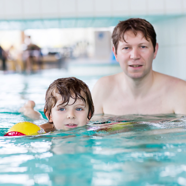Junger Vater bringt seinem kleinen Sohn das Schwimmen im Haus bei - Foto, Bild