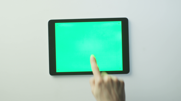 手は白いテーブルの上に緑色の画面を持つタブレットPCを置き、それを使用し始めています。モックアップの使用に最適 - 映像、動画