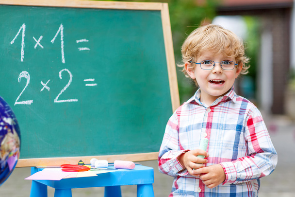 Cute little kid boy with glasses at blackboard practicing mathem - Photo, Image