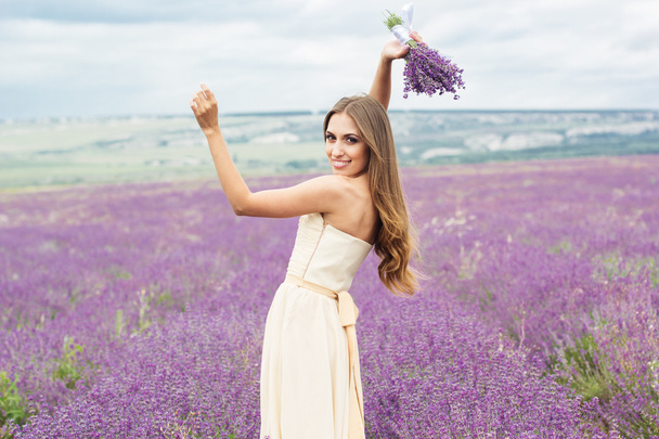 Pretty girl is wearing wedding dress at purple lavender field - Foto, afbeelding