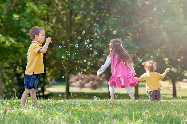 Three children in the park blowing soap bubbles and having fun - Foto, imagen