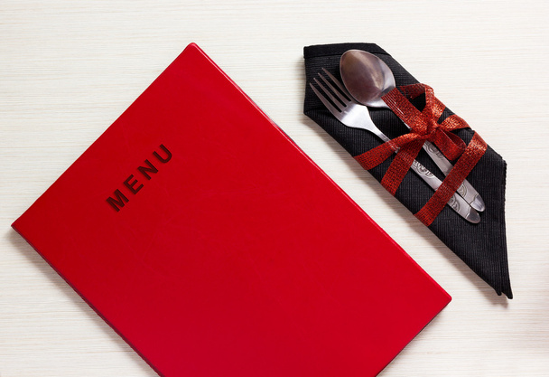 Посуда с красным бантом на черной салфетке рядом с меню
 - Фото, изображение