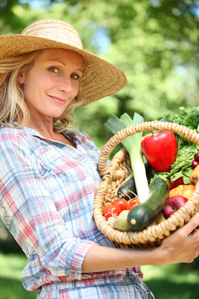 Woman with a straw hat holding basket of vegetables. - Foto, afbeelding
