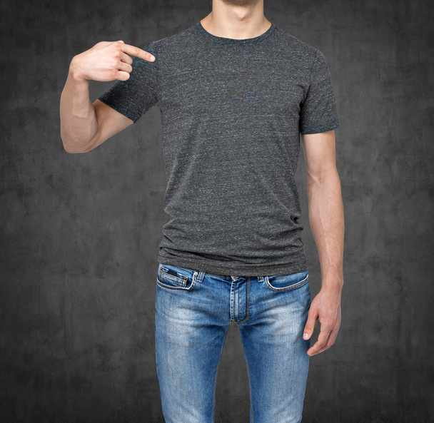 Close-up of a man pointing his finger on a blank grey t-shirt. Dark concrete background. - Foto, Imagen