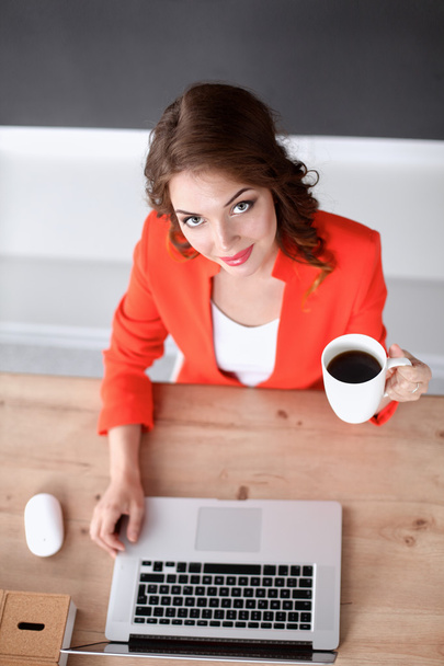 Ελκυστική γυναίκα που κάθεται στο γραφείο στο γραφείο, εργάζεται με φορητό υπολογιστή - Φωτογραφία, εικόνα