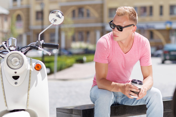 Handsome man sitting with coffee near his scooter  - Zdjęcie, obraz