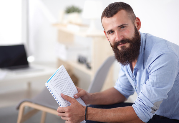 Young businessman sitting on chair with book in office - Photo, image