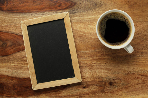 Cup of coffee on desk with blank chalkboard - Foto, imagen