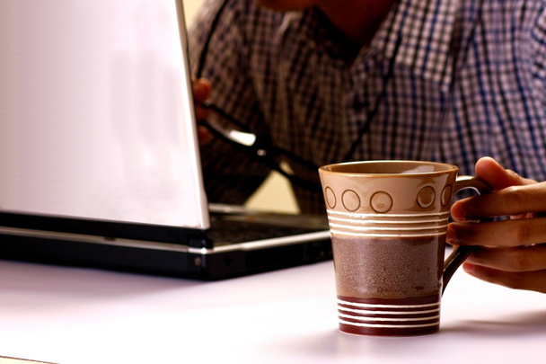 Tasse à café tenue par un homme travaillant sur un ordinateur portable en arrière-plan
 - Photo, image