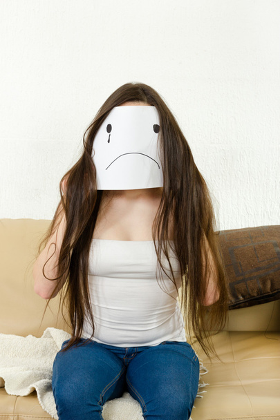 Adult girl cover her face with sad smile drawn on paper with one - Φωτογραφία, εικόνα