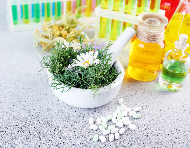 Herbs in mortar, test tubes and pills,  on table, on light background - Foto, afbeelding