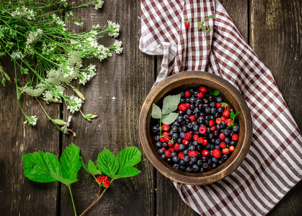 Wooden bowl with wild berries on dark wooden table.  - Foto, immagini
