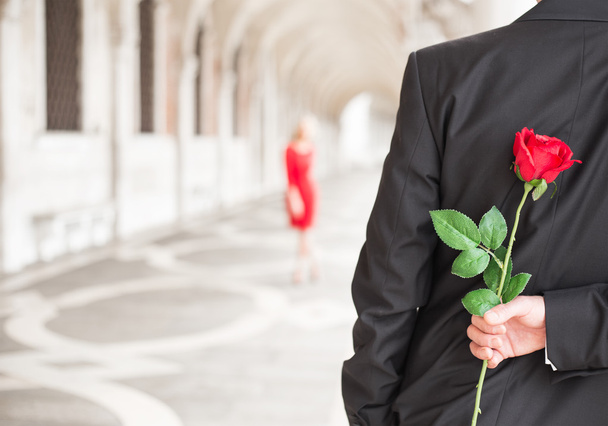 Mies odottaa treffejään punainen ruusu selän takana
 - Valokuva, kuva