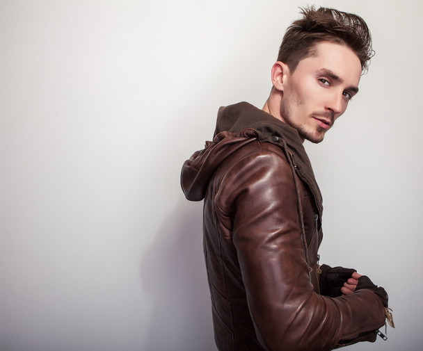 Привлекательный молодой человек в коричневой кожаной куртке позирует в студии
. - Фото, изображение