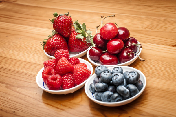 Маленькі миски з фруктами, що містять вишню, полуницю, чорницю та рабатку на дерев'яному столі
 - Фото, зображення