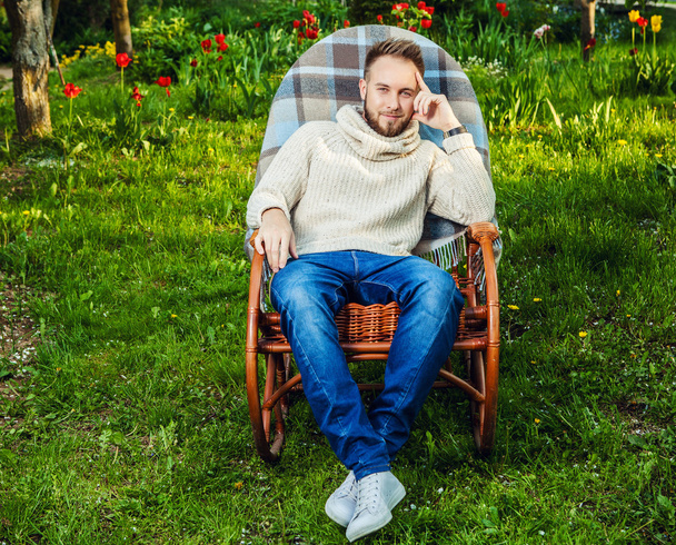 Handsome man relax in rocking-chair with plaid in a summer garden. - Foto, imagen
