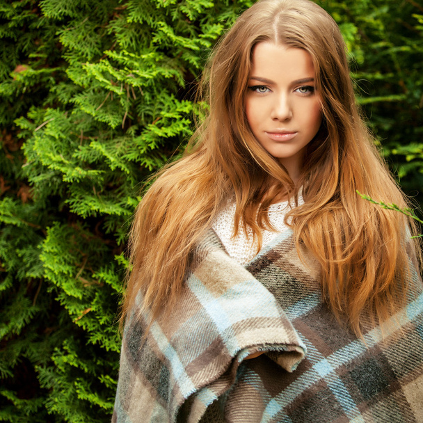 Outdoors portrait of beautiful young girl in casual white sweater & rolled in a plaid. - Photo, image
