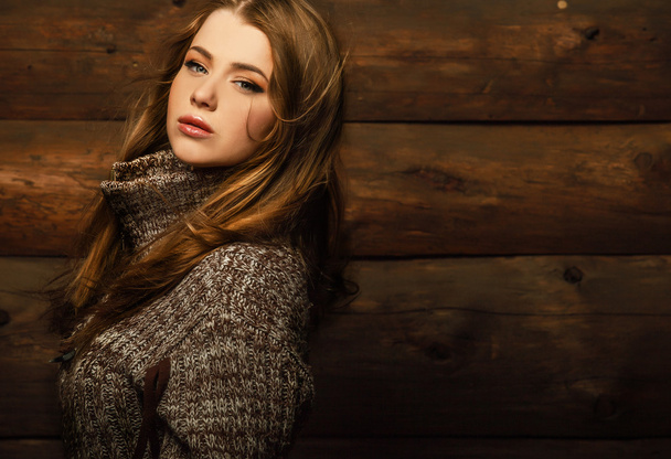 Young attractive girl in a brown sweater poses on wooden background. - Фото, зображення