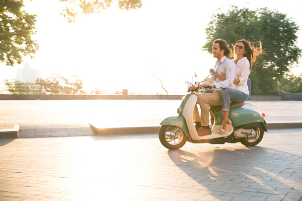 Happy young couple riding a scooter outdoors - Foto, imagen