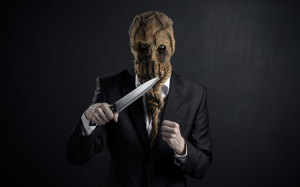 Fear and Halloween theme: a brutal killer in a mask holding a knife on a dark background in the studio - Φωτογραφία, εικόνα