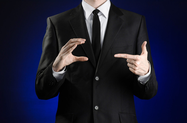 Businessman and gesture topic: a man in a black suit and white shirt showing gestures with hands on a dark blue background in studio isolated - 写真・画像