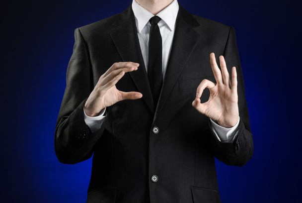 Businessman and gesture topic: a man in a black suit and white shirt showing gestures with hands on a dark blue background in studio isolated - Фото, изображение