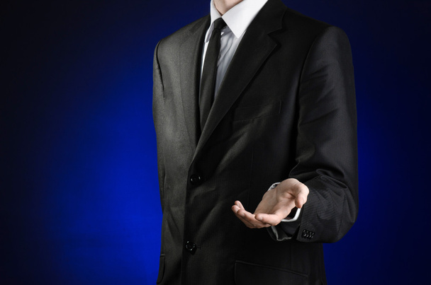 Businessman and gesture topic: a man in a black suit and white shirt holds up a hand against the dark blue isolated background in studio - 写真・画像