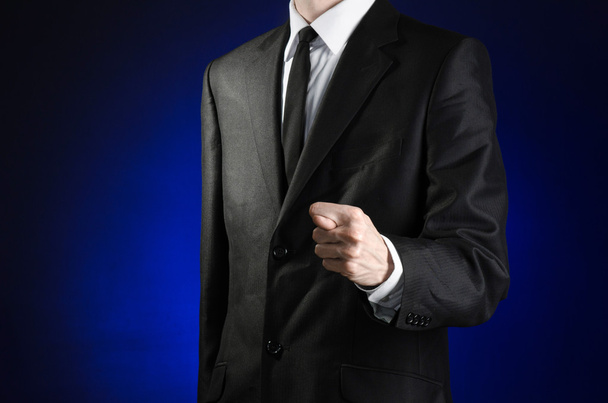Businessman and gesture topic: a man in a black suit and white shirt showing fig hand on a dark blue background in studio isolated - Foto, afbeelding