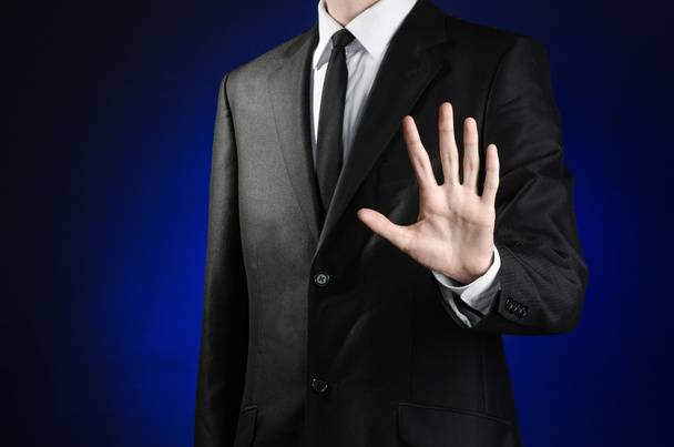 Businessman and gesture topic: a man in a black suit and white shirt showing gestures with hands palm against the dark blue isolated background in studio - 写真・画像