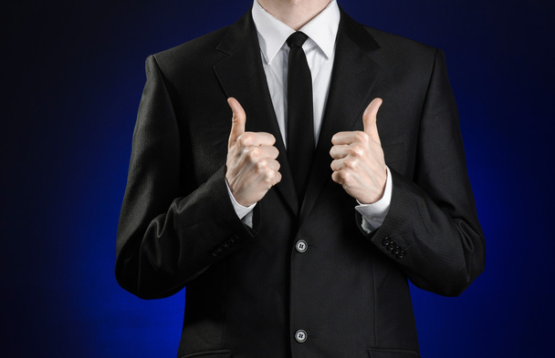 Businessman and gesture topic: a man in a black suit and white shirt showing hand gestures a thumbs-up on a dark blue background in studio isolated - Fotoğraf, Görsel