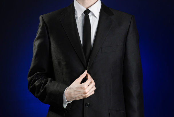 Businessman and gesture topic: a man in a black suit and white shirt correcting a jacket and tie on a dark blue background in studio isolated - Fotografie, Obrázek