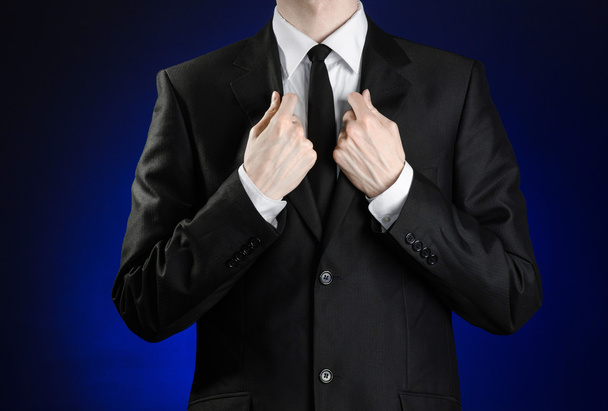 Businessman and gesture topic: a man in a black suit and white shirt correcting a jacket and tie on a dark blue background in studio isolated - Photo, Image