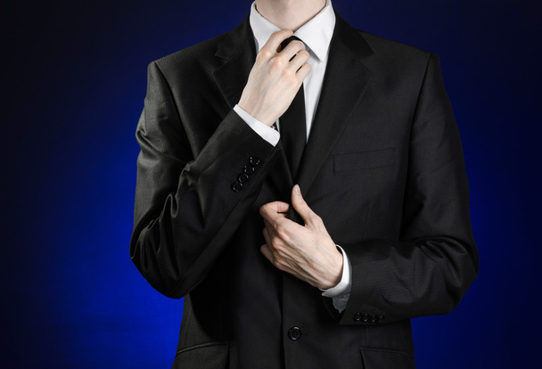 Businessman and gesture topic: a man in a black suit and white shirt correcting a jacket and tie on a dark blue background in studio isolated - Foto, Bild