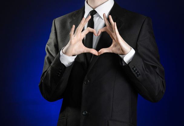 Businessman and gesture topic: a man in a black suit and white shirt holding his hands in a sign of heart on a dark blue background in studio isolated - Foto, Bild