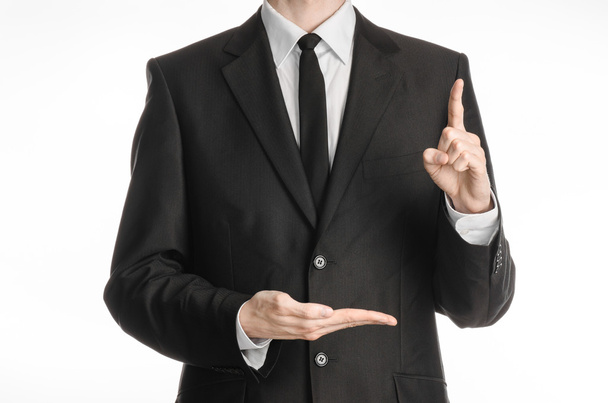 Businessman and gesture topic: a man in a black suit with a tie shows the left hand index finger up and keeps his right hand on a white isolated background in studio - Foto, Imagen