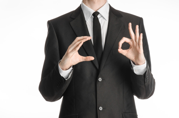 Geschäftsmann und Gestenthema: Ein Mann im schwarzen Anzug und Krawatte hält seine rechte Hand und die Linke zeigt ein Zeichen des Okay auf weißem Hintergrund im Studio - Foto, Bild