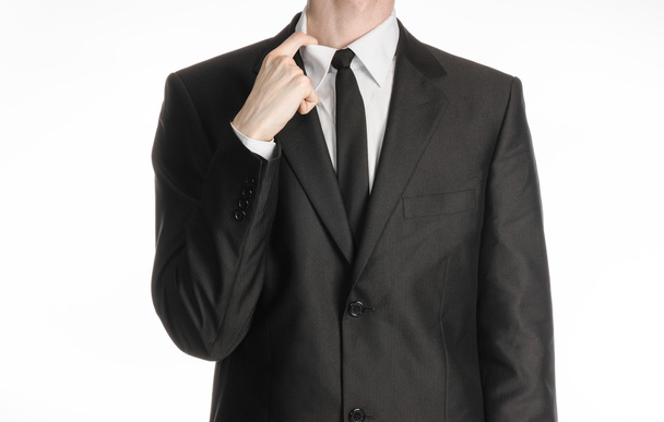 Businessman and gesture topic: a man in a black suit and tie holding a hand to his shirt collar isolated on a white background in studio - Foto, Imagem