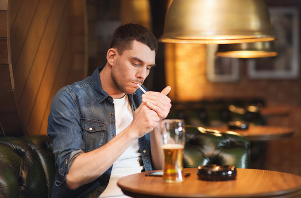 man drinking beer and smoking cigarette at bar - Фото, изображение