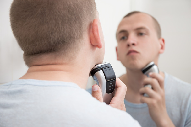 Молодой человек в зеркале бритья с электробритвой
 - Фото, изображение