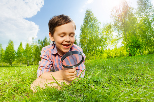 Happy small boy searches with magnifier - Foto, afbeelding