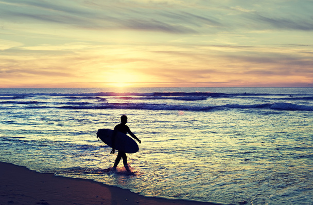 Серфер ходить на пляжі під час заходу сонця
 - Фото, зображення